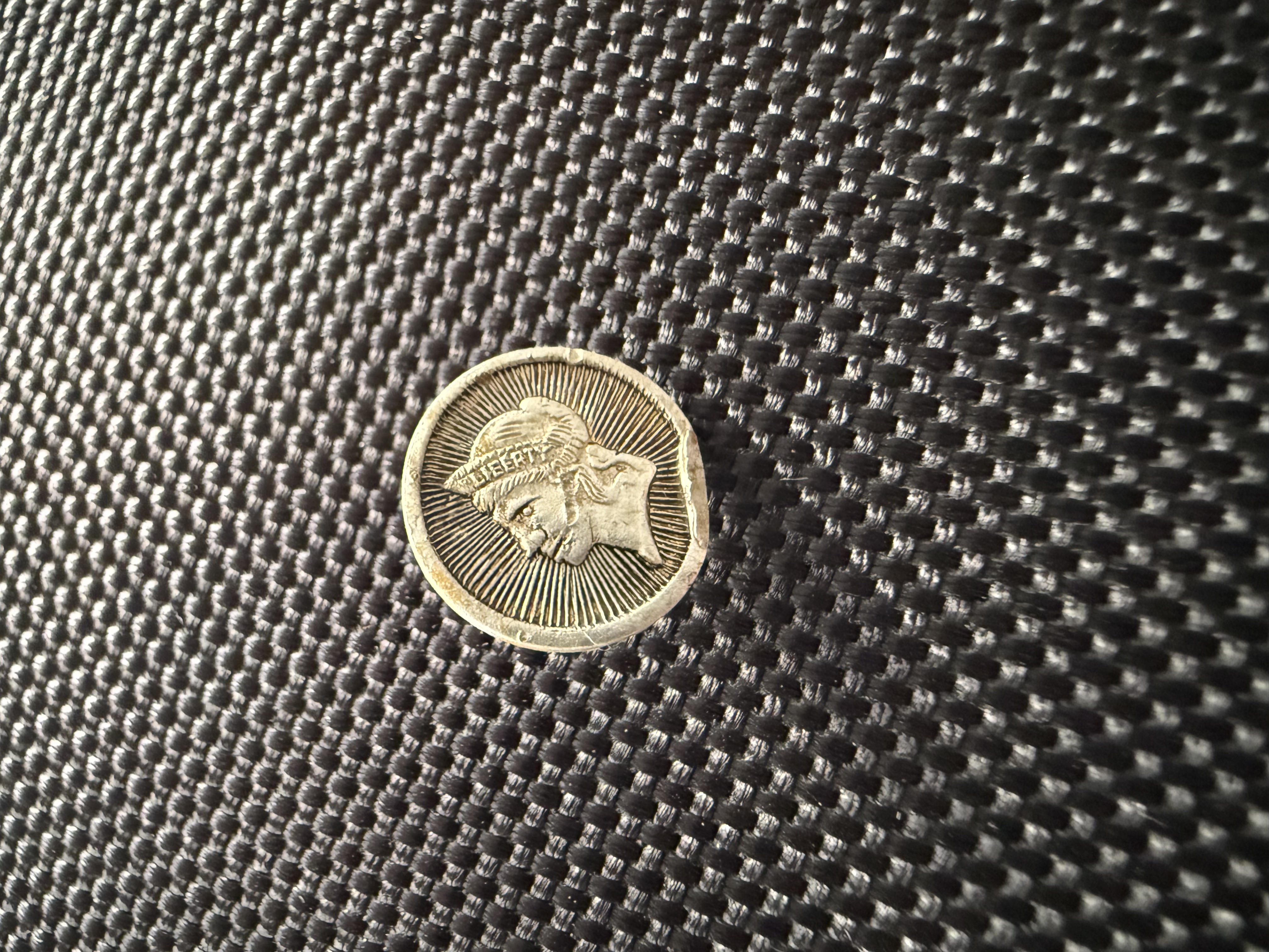 Small silver-toned button with raised classical portrait inscribed LIBERTY surrounded by radiating sunburst pattern, found by metal detecting