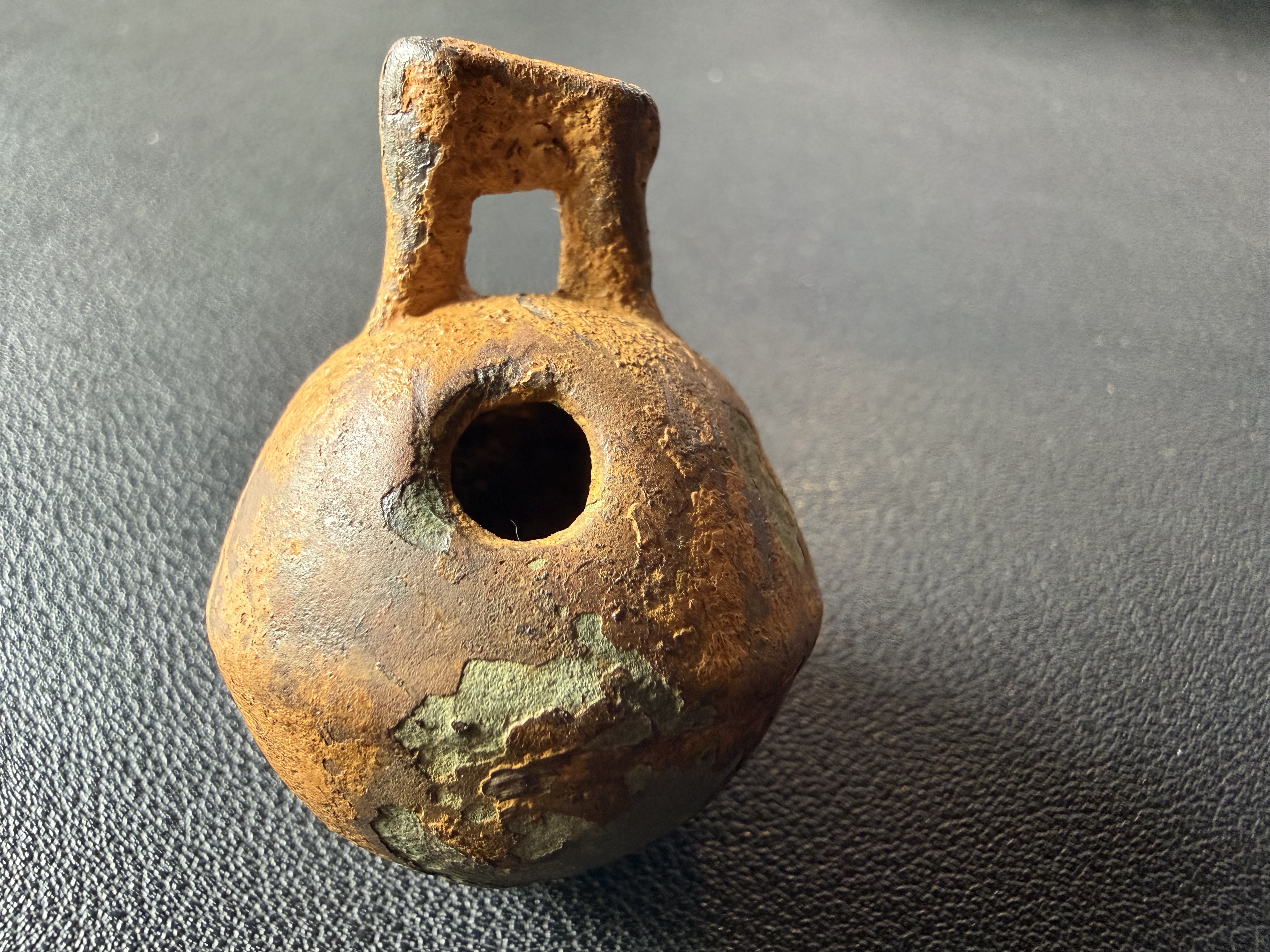 Corroded copper-alloy vessel with square handle loop, found by metal detecting