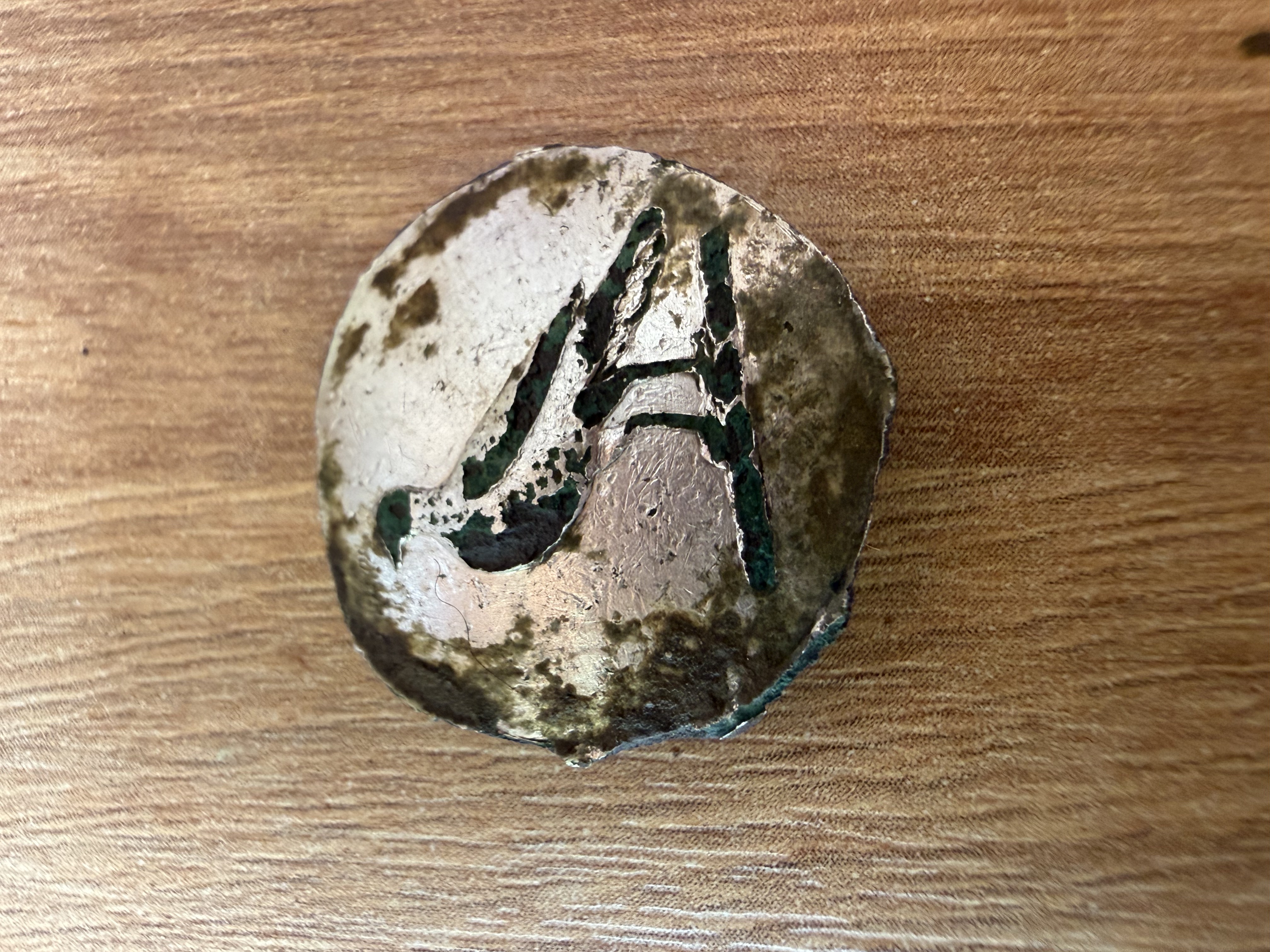 Domed copper-alloy button with corroded surface revealing a raised letter A monogram beneath green verdigris patination, found by metal detecting