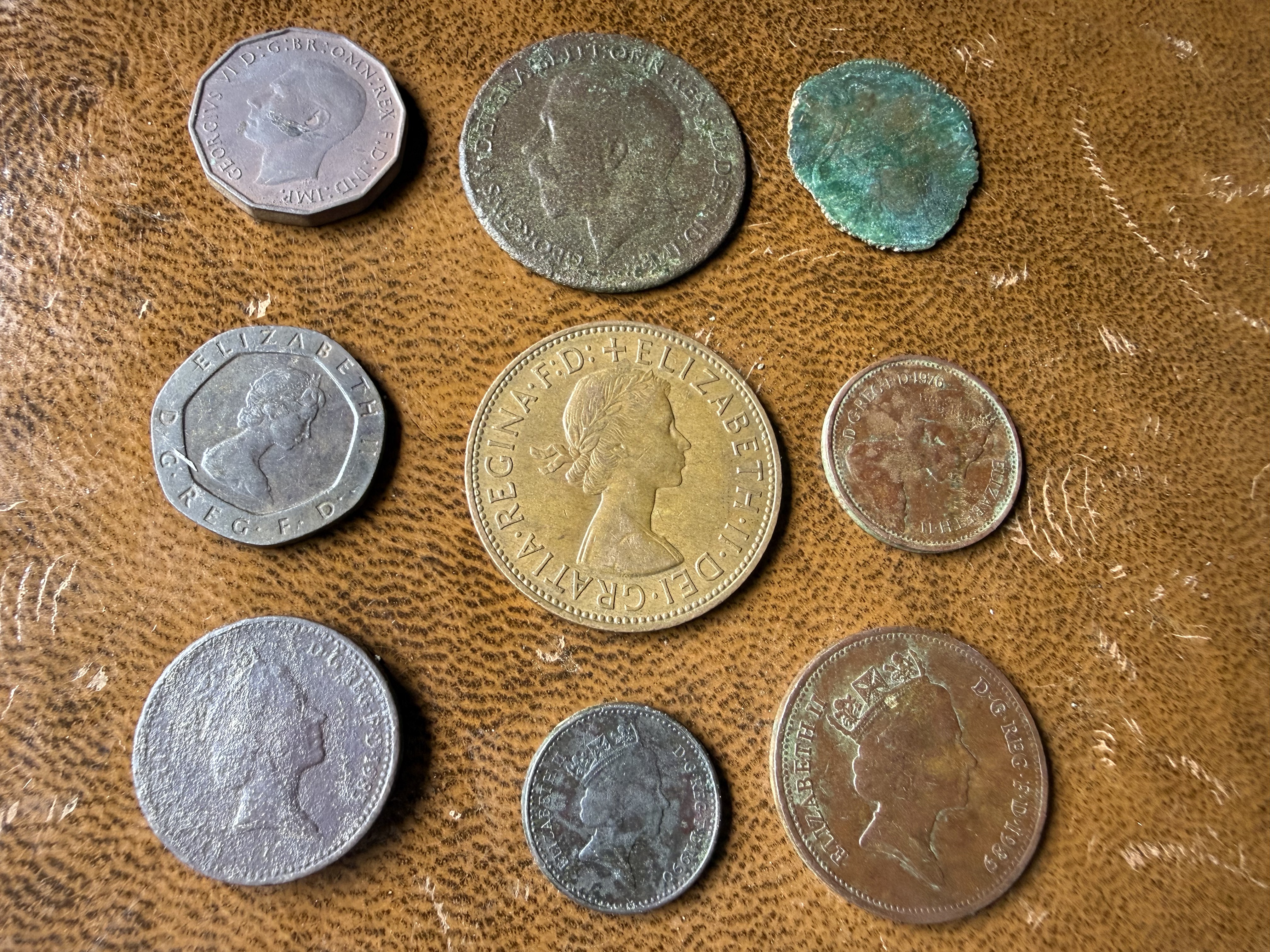 Collection of eight coins on leather including George VI threepenny bit, Elizabeth II florin, and corroded ancient coin with verdigris, found by metal detecting